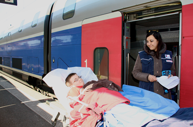 Photo d'un enfant souriant sur un brancard devant la voiture d'un train